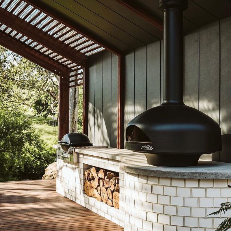 Polito Giotto Wood Fired Oven With Bench Stand in Black in an outdoor kitchen with roof