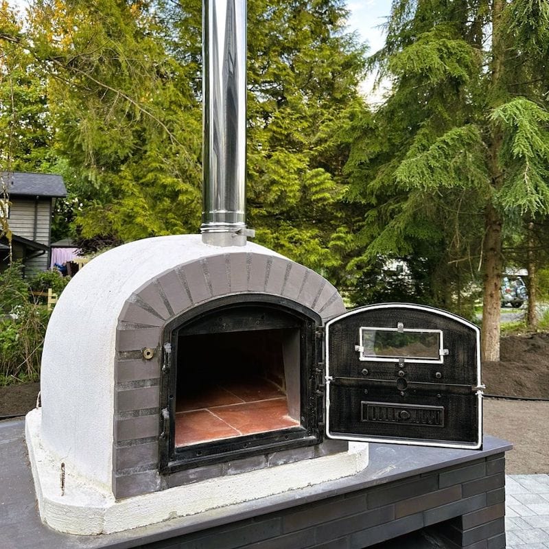 A close up of the Lume Alto Brick Wood Fired Oven sitting on a black outdoor kitchen countertop with the doors open