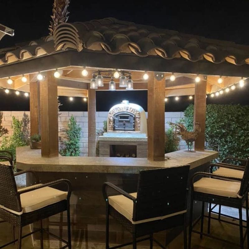 Ventura Sierra Brick Oven set on an outdoor kitchen counter under a small bar pergola countertop with lights